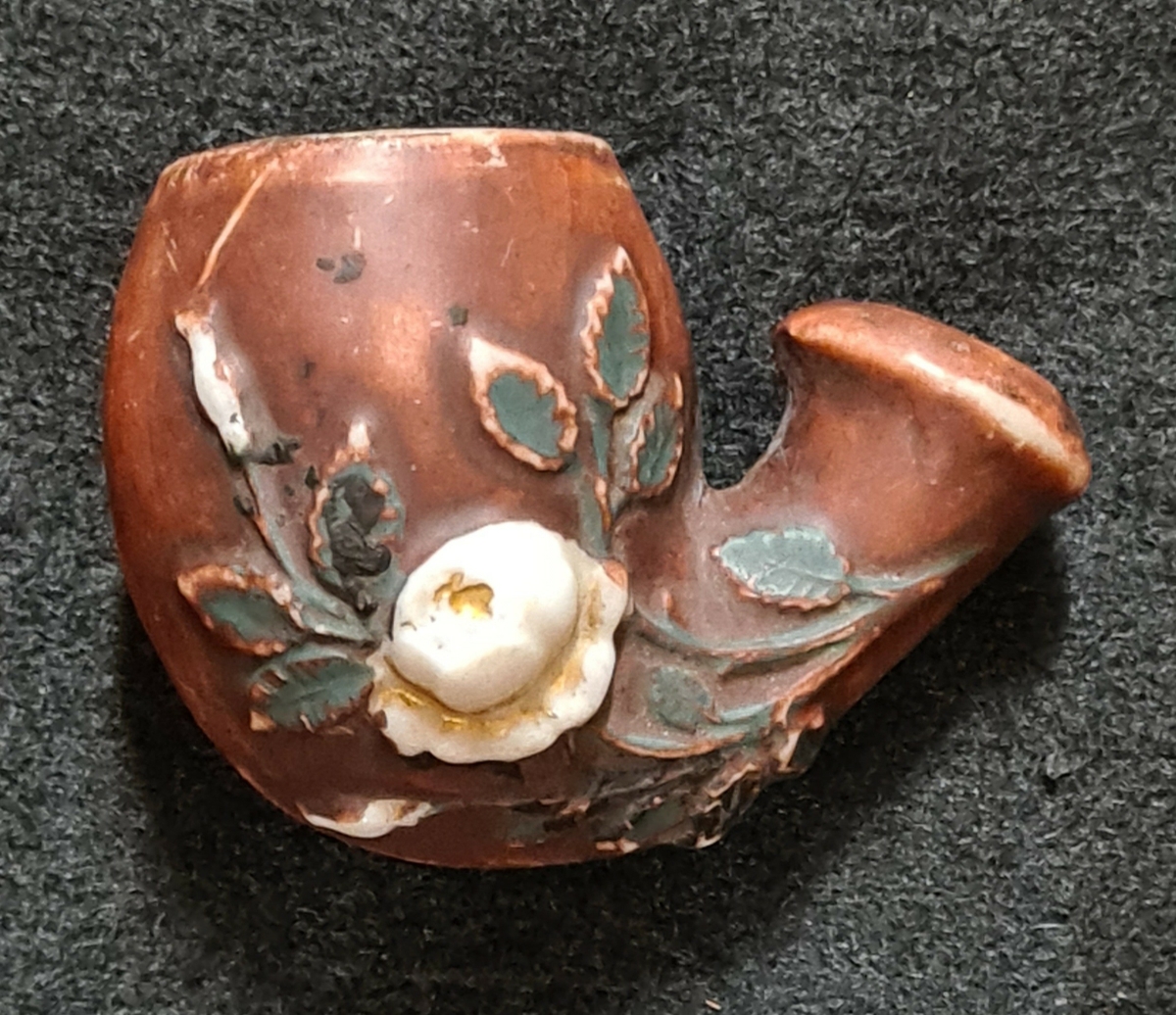 Piphuvud i porslin, brunt med vita blommor och gröna blad i relief.