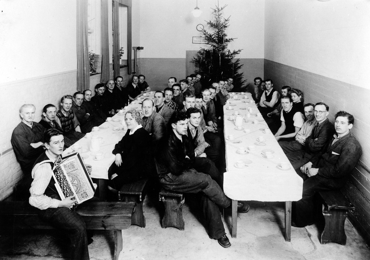 Alingsås bomullsväveri, nya fabriken. 
B-skiftets julfest. Två dukade långbord med män och kvinnor och en man med dragspel.
