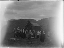 Gruppe mennesker på fjellet foran laftet bygg. Muligens dans