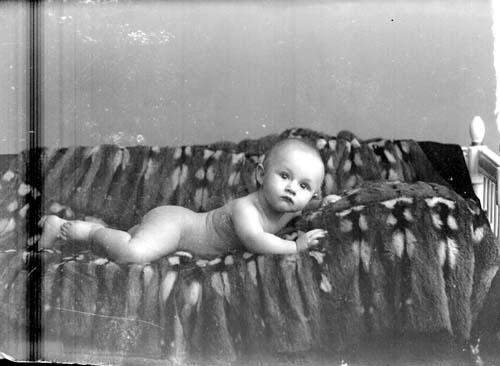 Ett spädbarn, en pojk, ligger naken på en päls i en soffa.