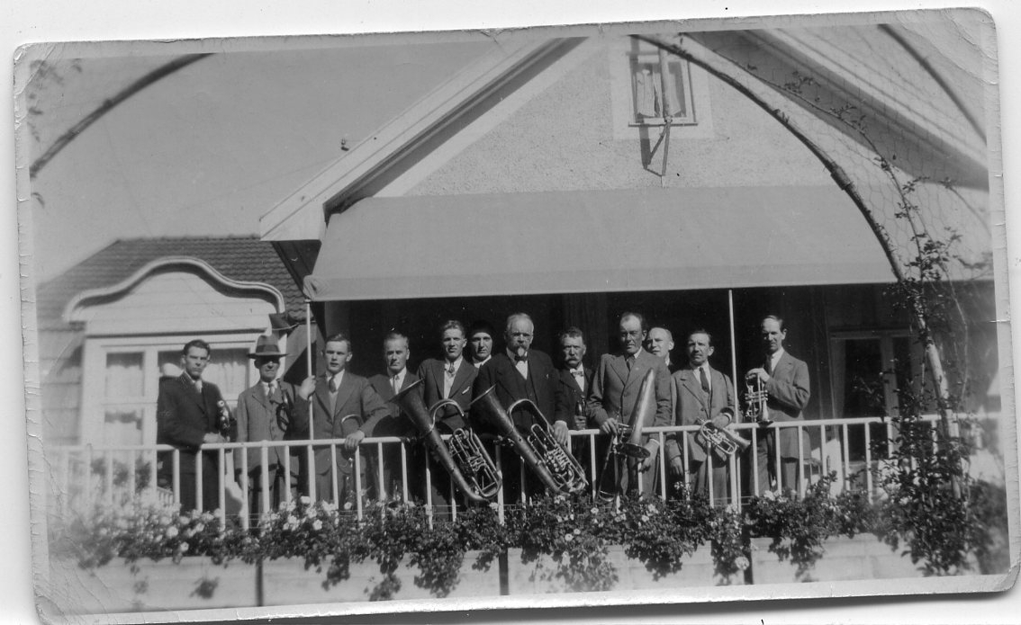 Tolv män med blåsinstrument uppställda på en balkong.