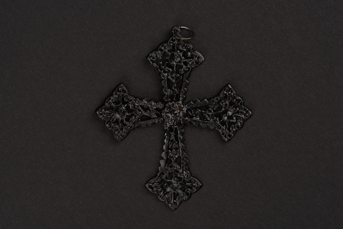 Hänge till halsband i form av ett kors.
Korset är av utsirat svart gjutjärn med rombformade avslut i nygotisk stil. I mitten sitter en oval förnicklad platta med två änglahuvuden i gjutjärn.