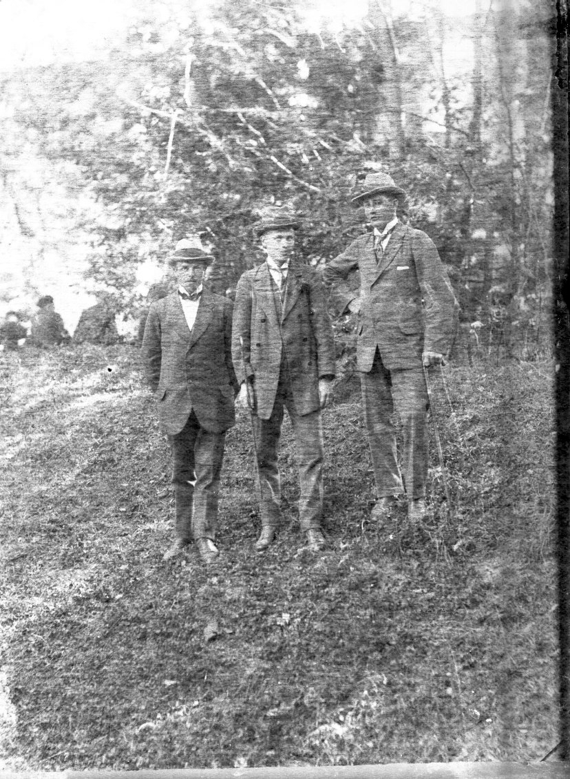 Tre unga män med hatt och spatserkäpp står på en grässlänt, troligen i närheten av Visingsborgs slottsruin. Det är sommar.