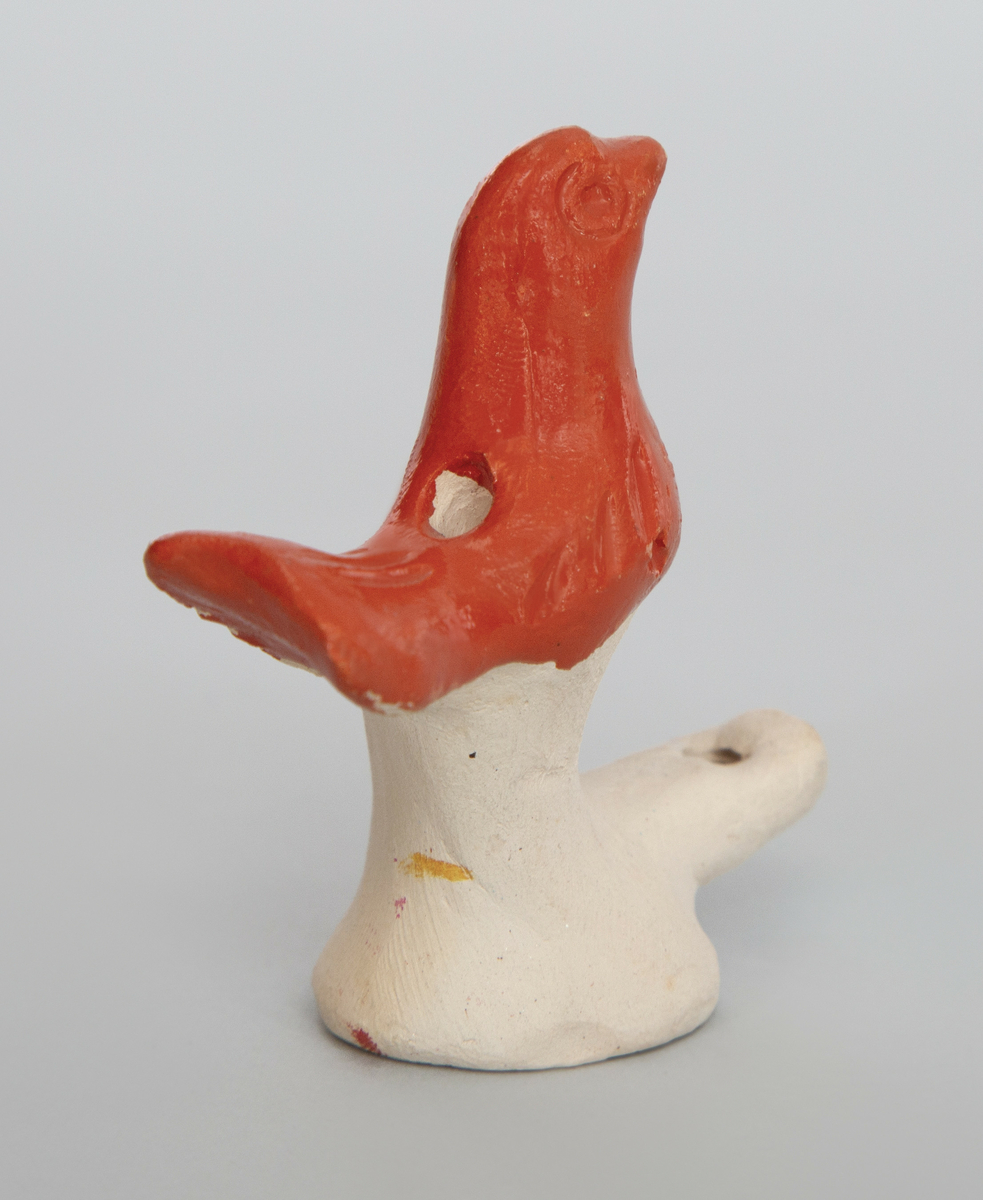 Spaltefløyte i keramikk i form av en liten fugl på en sokkel. Fuglen orange glasert, selve sokkelen uglasert.
Spalte og labium i sokkelen.
Ingen fingerhull.