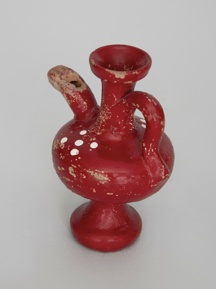 Spaltefløyte. Vannfløyte av keramikk formet som en liten vase med stett, klokke og hals, tut og hank.
Halsen er åpen øverst for påfylling av vann. Spalte og labium i tuten.
Utvendig dekorert med rød glasur med hvit prikkdekor.

