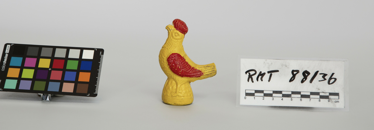 Spaltefløyte av keramikk. Formet som en hane. Støpt i to halvdeler. Malt gul med røde vinger og kam.
Spalte og labium i stjerten. Ett fingerhull.