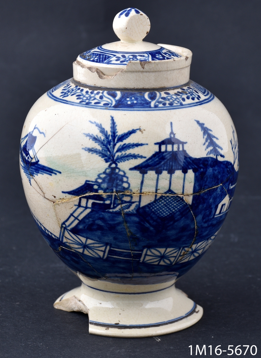 Rund urna med lock och handmålad dekor i blått, föreställande landskap och hus.