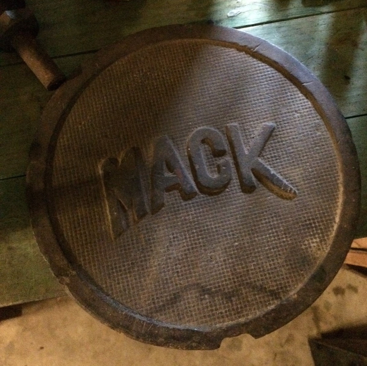 Rund skylt, alternativt ett lock, av gjutjärn med texten MACK på räfflad botten.