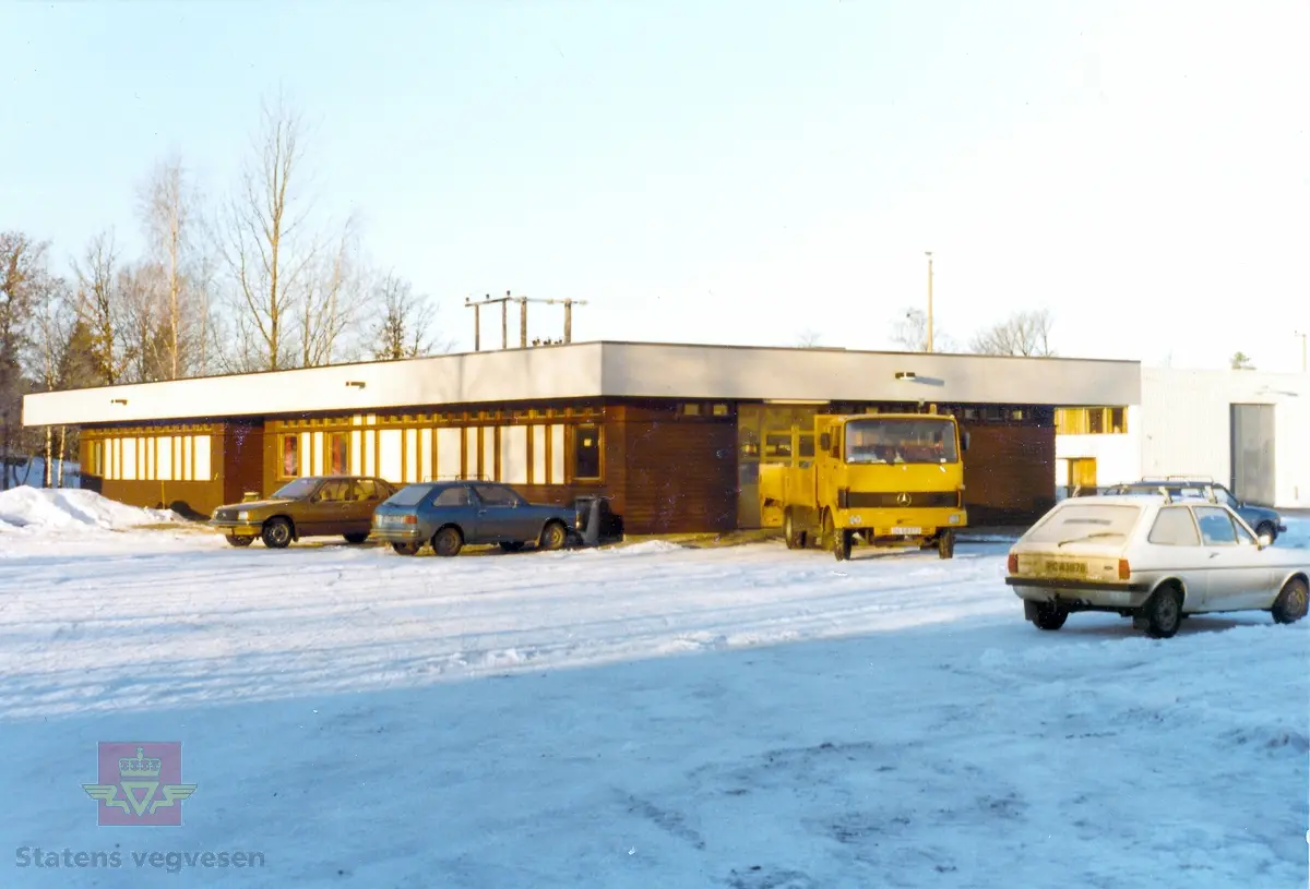 Vinterbilde av Statens vegvesens laboratorium på Skarpnes i Arendal. På gårdsplassen står flere biler parkert. Blant annet en 1978 modell  Mercedes-Benz LP 809-36 fra Statens vegvesen. En 1979 modell hvit Ford Fiesta 1.1. personbil.