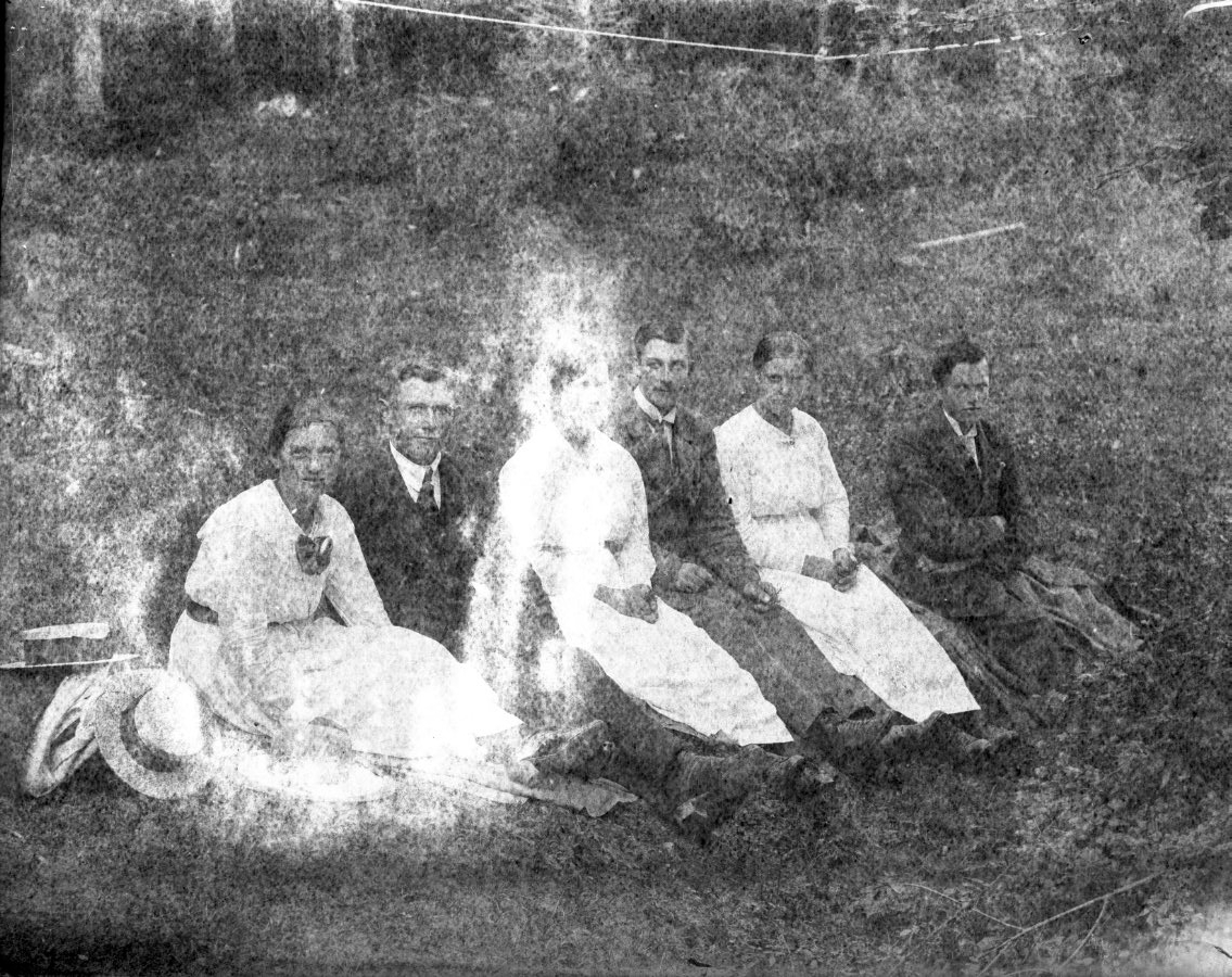 Tre kvinnor och tre män sitter på en slänt, de har lagt hattarna intill sig.