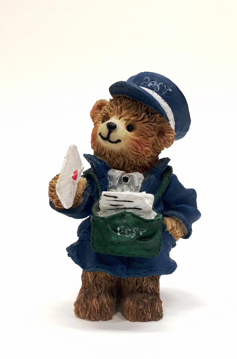 Figurin förställande en björn i uniform med mössa och brevbärarväska. Björnen håller ett brev.