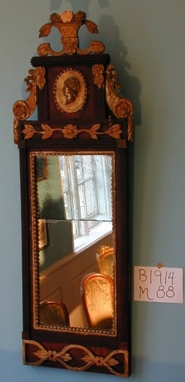 Speil Fra protokollen: Speil i Ludv. 16's stil. Rammen har brun træfarve med forgyldte ornamenter. I topstykket en medaljon med ansigt i höit relief.