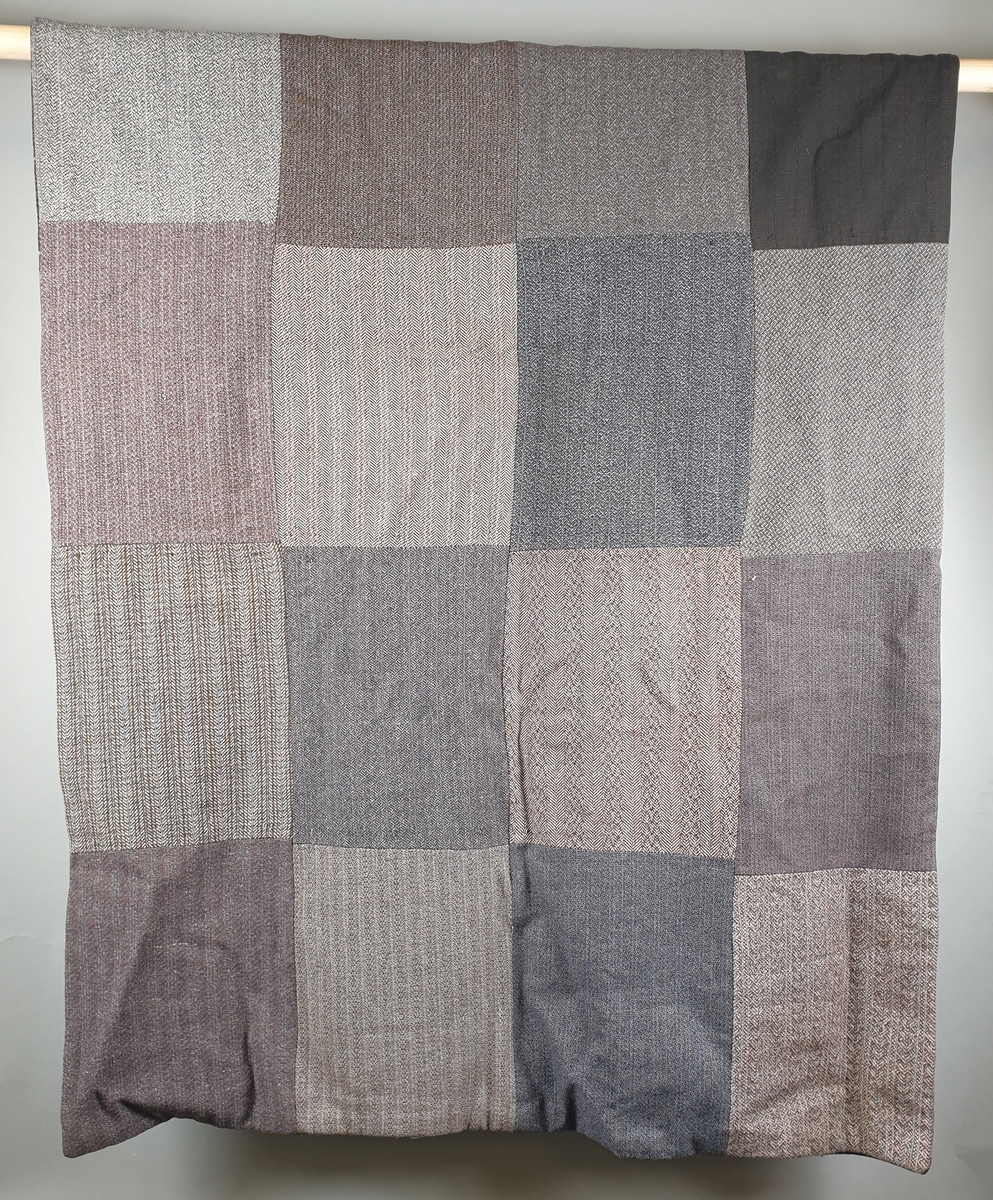 Lappeteppe satt sammen av flere stoffstykker av ull. Teppet er dobbelt og på forsiden er det brodert diagonale striper med lyseblått ullgarn.
