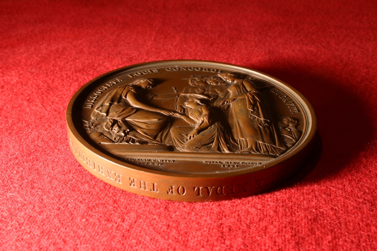 Bronsemedalje fra 1851. På adversen dronning Victoria og prins Albert i profil mot venstre. På reversen er hovedmotivet at en kvinnelig guddom(?) en laurbærkrans til en annen kvinne.