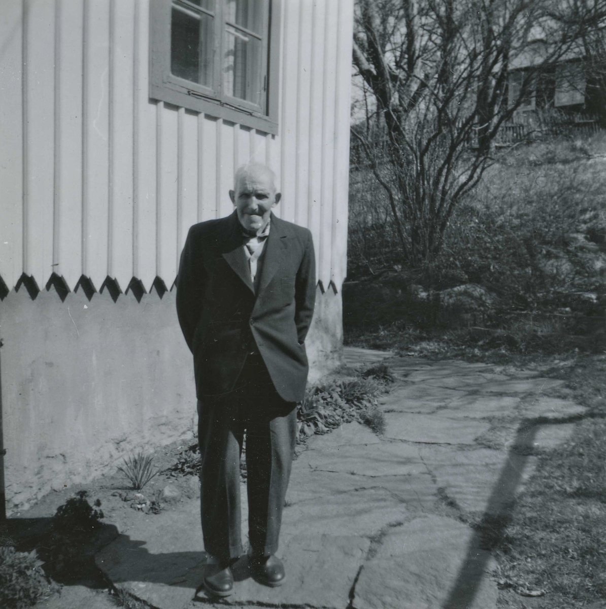 Robert Pettersson (född i Lindome 1886, avliden 1968 på Brattåshemmet) står utanför Börjessons hus på Norra Kyrkvägen 1/Lugnet 1 år 1957. I bakgrunden till höger ses Johannes Bengtssons Mekaniska verkstad. Robert arbetade som dräng på Ekans gård från 1912.