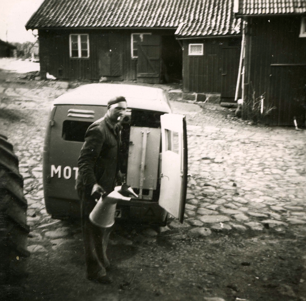 Gårdsplanen vid Ekans gård, Ekan 1:1 år 1953. Traktorreparatören Malte med en cigarett i munnen och en oljekanna i handen. 
Relaterat motiv: A1147.