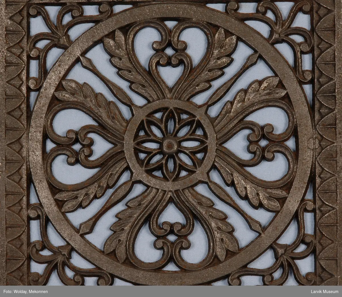 Symetrisk gjennombrudt blomster-ornamentikk i en sirkel, ornamentikk i hjørnene avsluttes med en bord-ramme