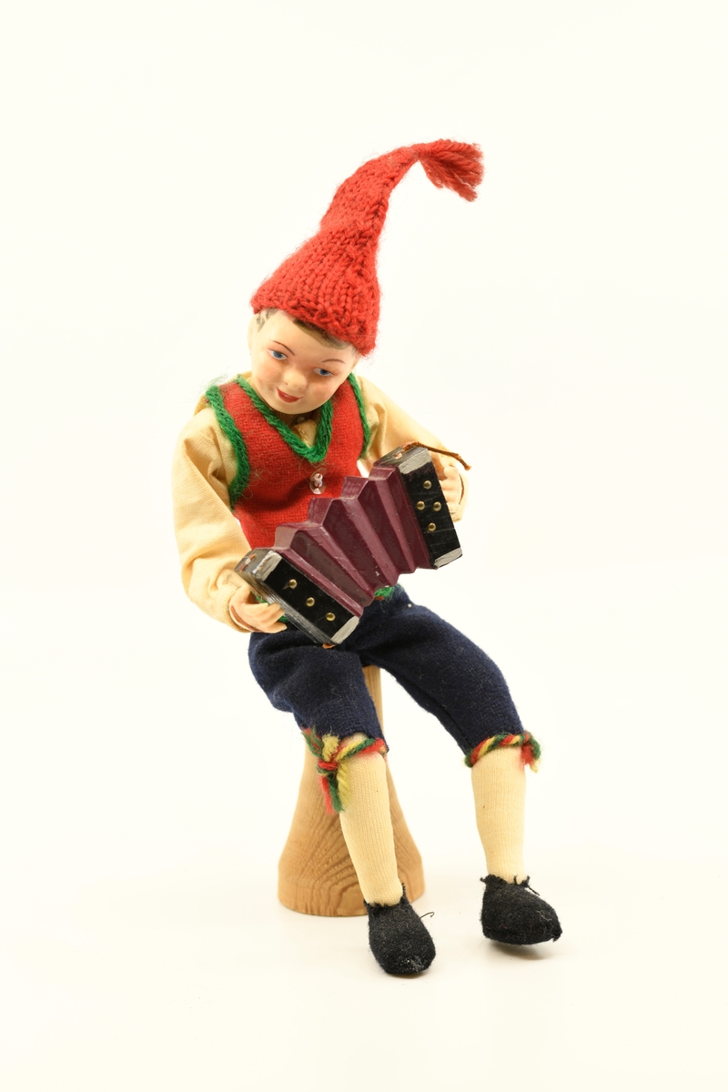 Dukke som forestiller mann som sitter på en "stubbe" og spiller på trekkspill.
