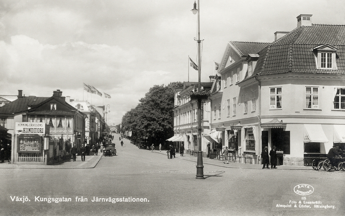 Kungsgatan, Växjö, från söder, vid korsningen mot Norra Järnvägsgatan, 1930. 
Till vänster ser man en del av husen i kvarteren Magnus Smek och Unaman, till höger hörnhuset i kvarteret Linné m.m..