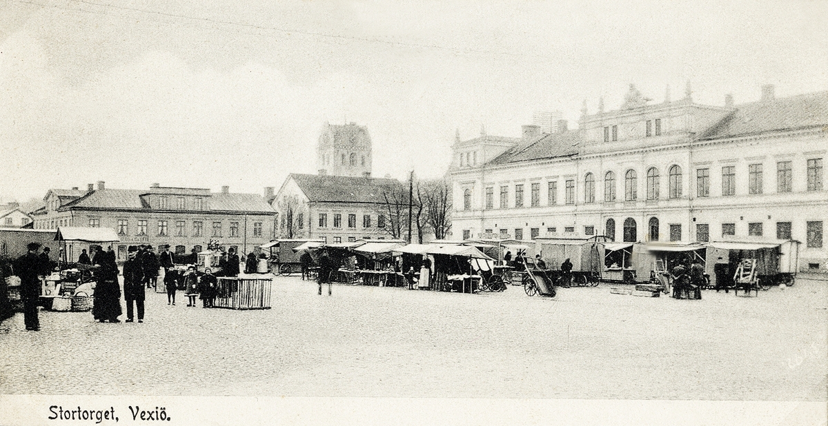 Stortorget, Växjö mot sydost, en marknadsdag. Tidigt 1900-tal.
Man ser några av husen längs Kronobergsgatan (kv. Lejonet) och till vänster tronar stadshuset (senare en del 
av stadshotellet). I bakgrunden syns domkyrkans torn.