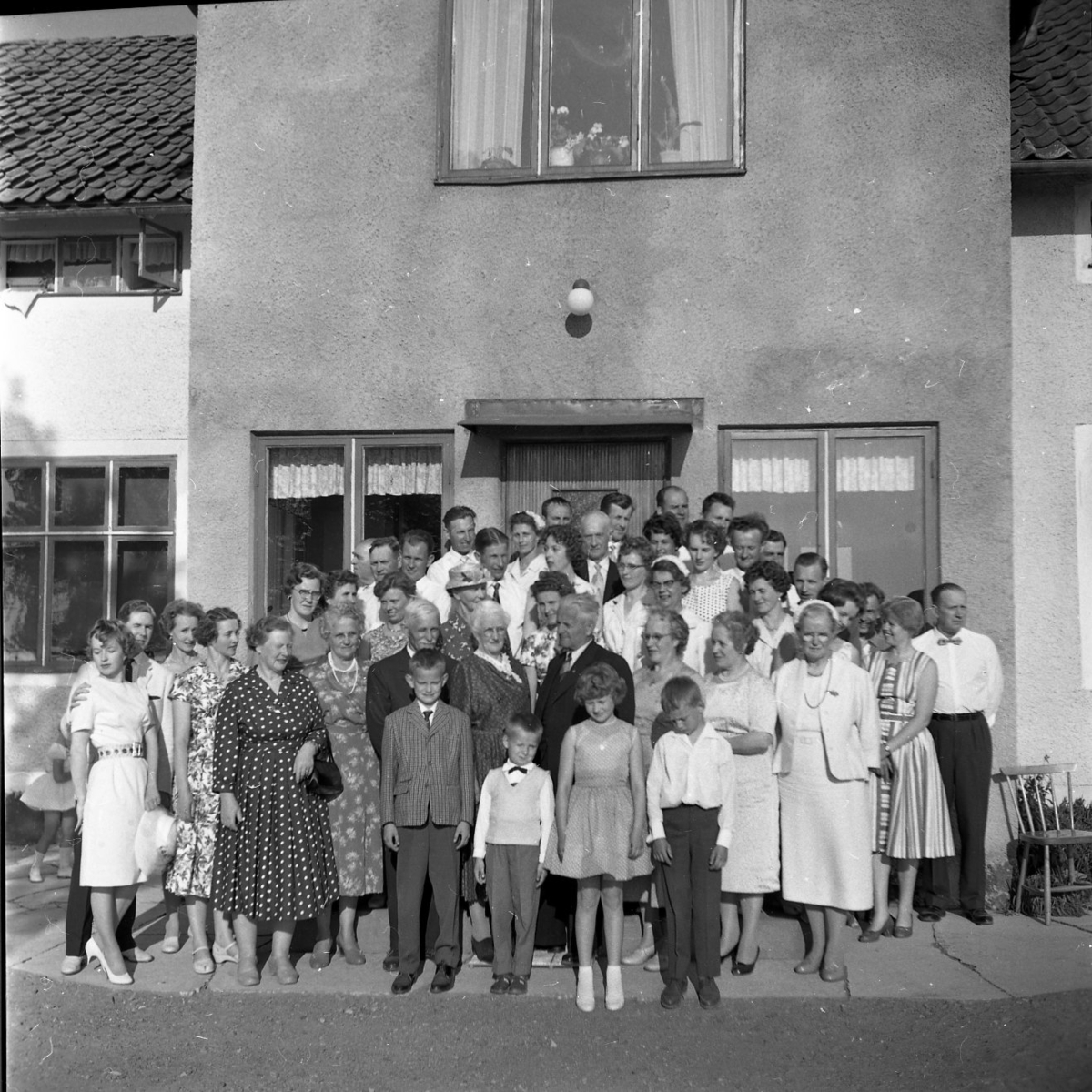 Släktmöte 1960. En stor skara människor, både barn och vuxna står uppställda framför ett hus med putsad fasad.