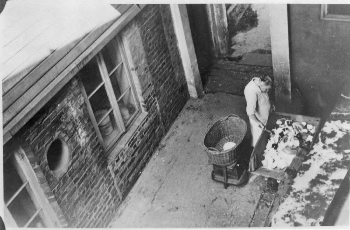 Fayancefabrikken, ca. 1950. Maria Terland fra sorterkjelleren knuser vraket steintøy før det blir dumpet på gruset.