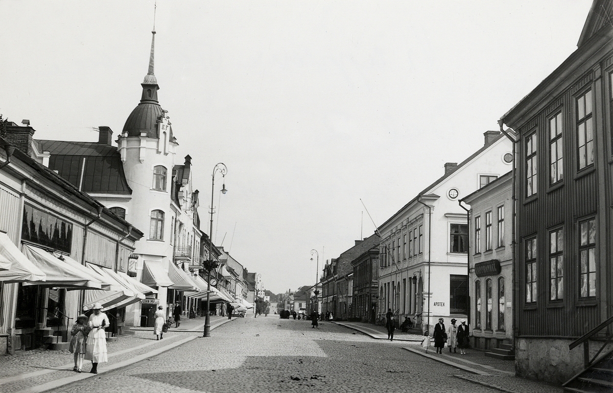 Storgatan vid korsningen mot Bäckgatan, ca 1920-1925, med vy mot öster och Stortorget. 
Närmast i bild kvarteret Nunnan, följt av kvarteret Klostret med familjen Feuks fastighet, till höger kvarteret Stormen, följt av kvarteret Blenda med apoteket i hörnet.