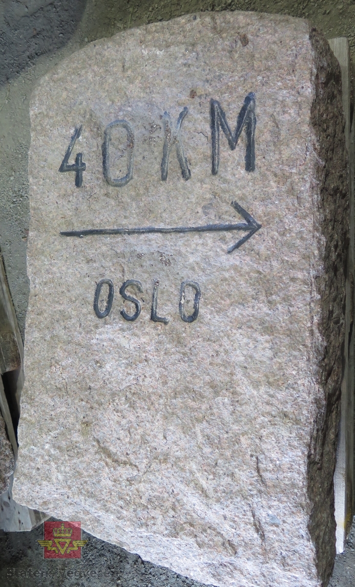 Grå-rød granittstein med teksten "40 KM TIL OSLO". Teksten er hugget inn i steinen og deretter malt svart.