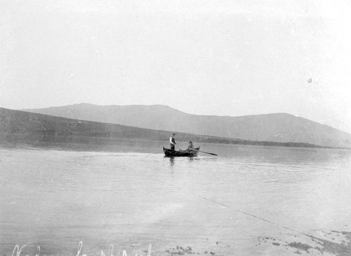 To menn i ein robåt som er ute på eit vatn og fiskar.