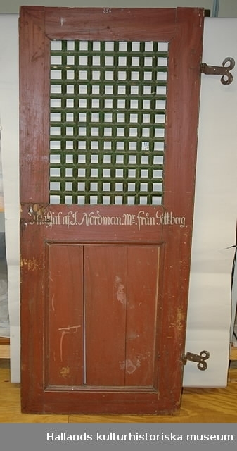 Dörr av trä med rött och grönt gallerverk i överstycket. Märkning: "1748 PASTORE CAROLO BRAG" och inskrift: "C Brag 1748"