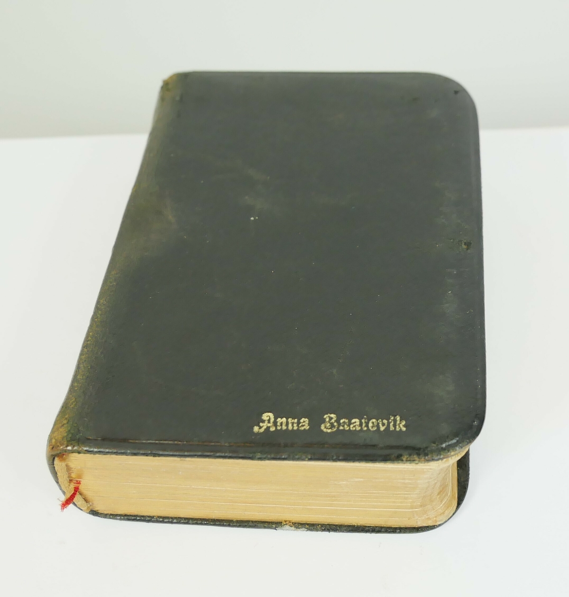 Rektangulær salmebok i svart skinn med forgylte sider. Boken ligger i en rektangulær beholder av svart kartong. 