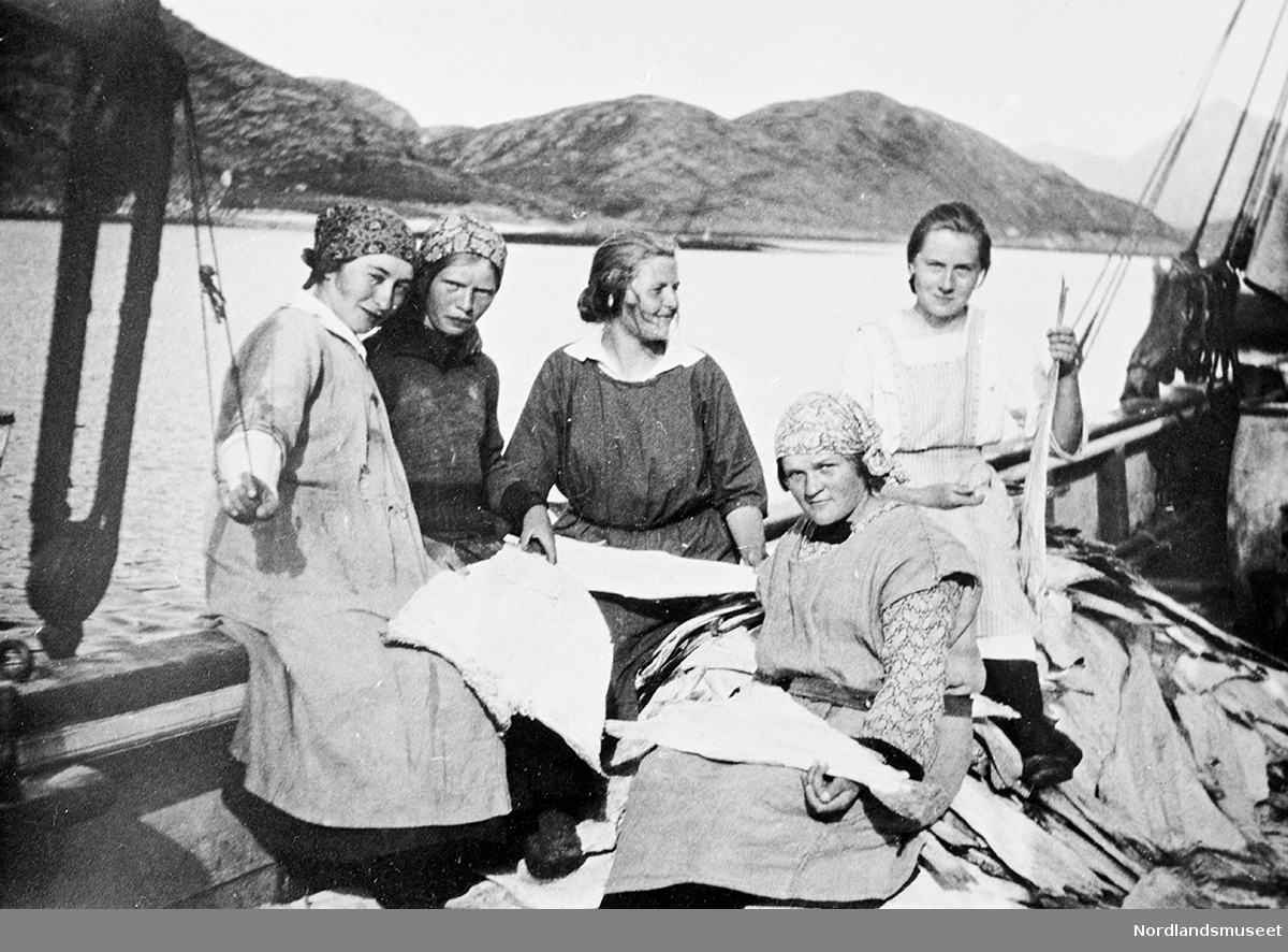 5 damer arbeider med klippfisk ombord i en båt.