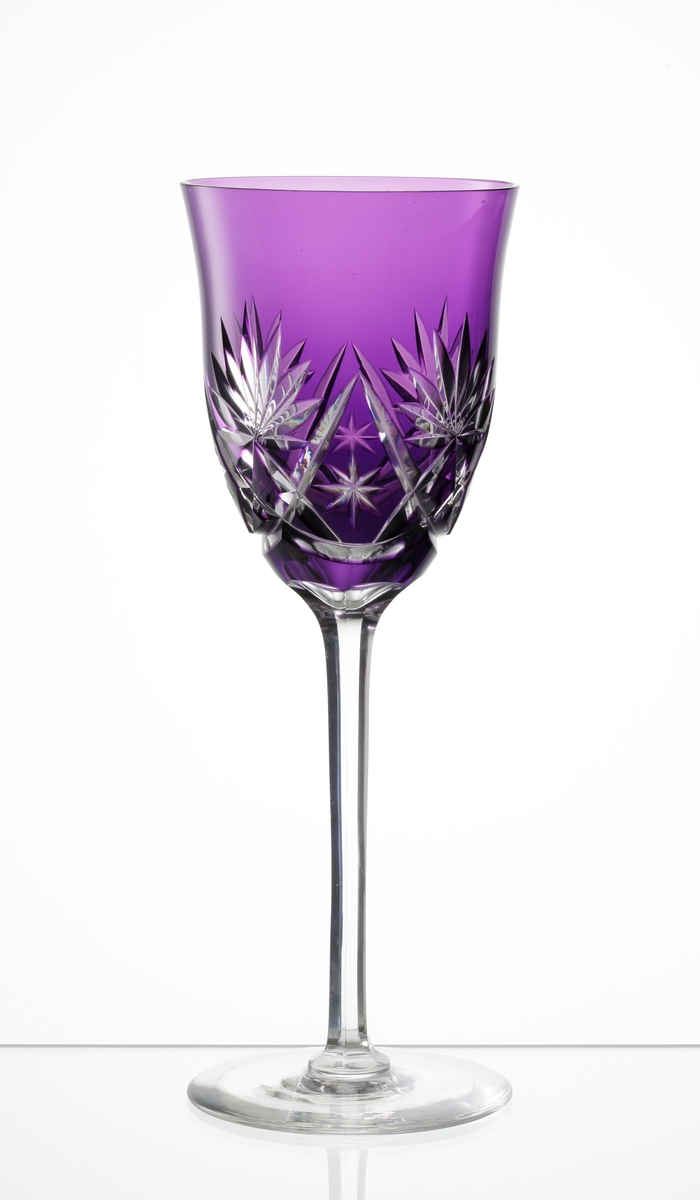 Design: Okänd. 
Rhenvinsglas, vid klockformad lila kupa med skärslipad dekor. Facettslipat högt ben med slät fot.