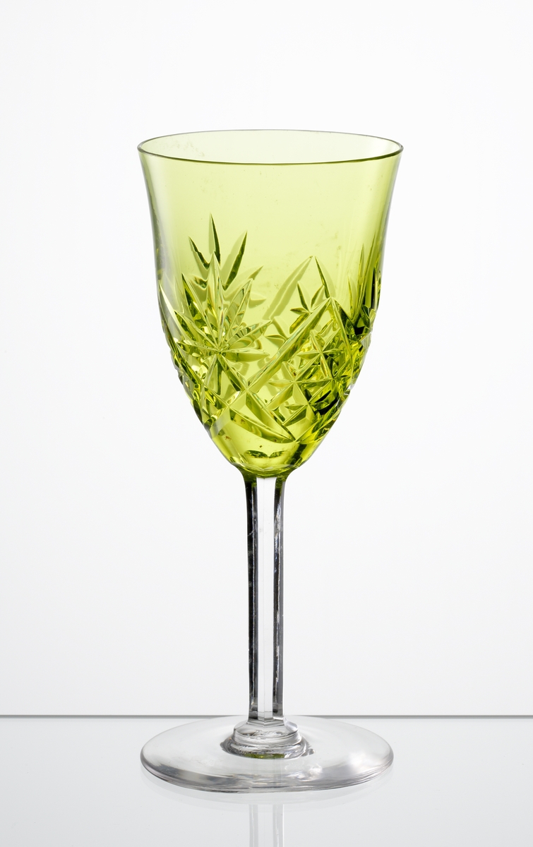 Design: Okänd. 
Vitvinsglas, svagt klockformad, gulgrön kupa med skärslipad dekor. Högt fasettslipat ben med slät fot.