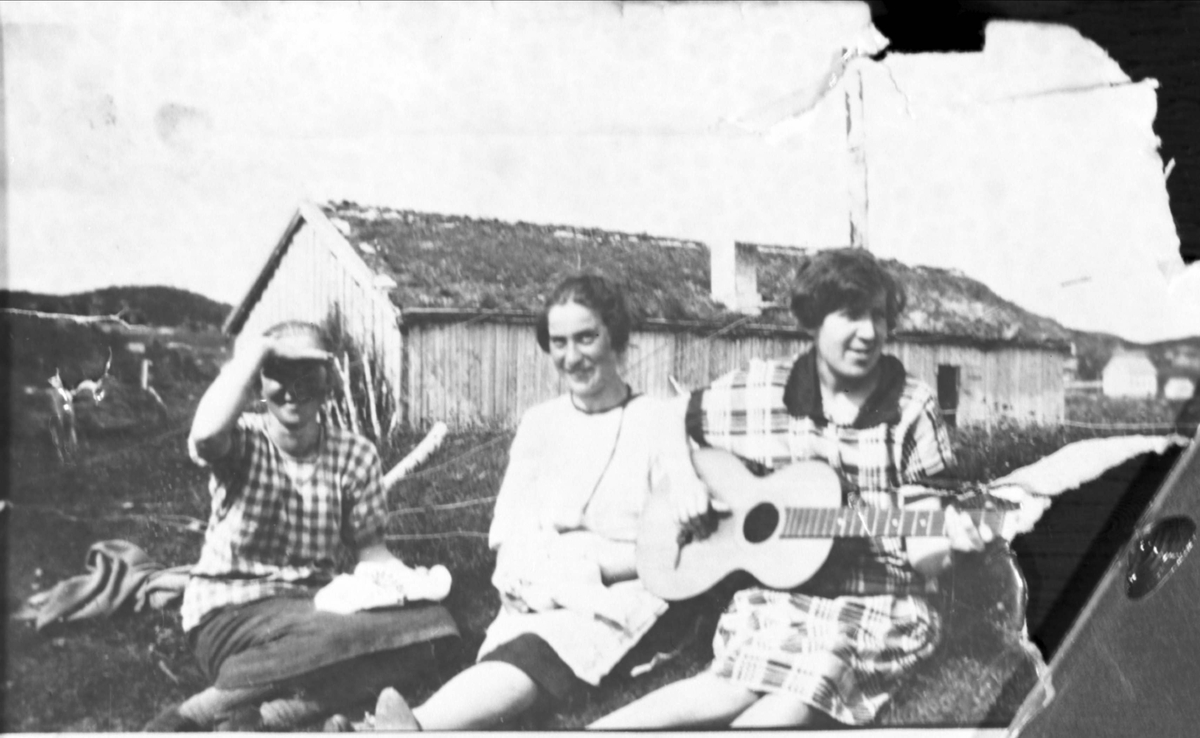 Amatørportrett av tre kvinner sittende på et gårdstun, den ene med gitar.