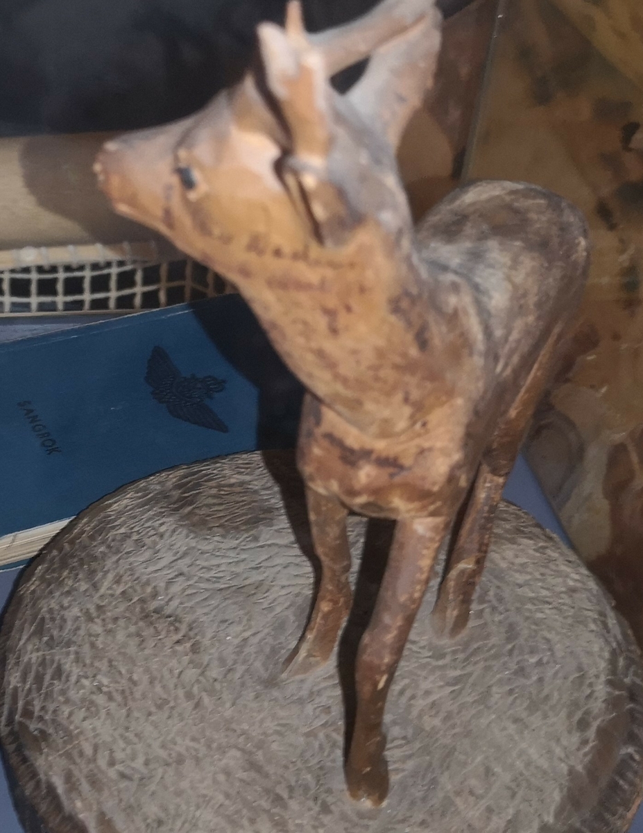 Filigran treskulptur som er skjært ut av et stykke treverk. Skulpturen viser en ung bukk med gevir. Bukken står på en sokkel. På bukken har flere soldater signert med blekk. Soldatene var på training i Little Norway (Canada).