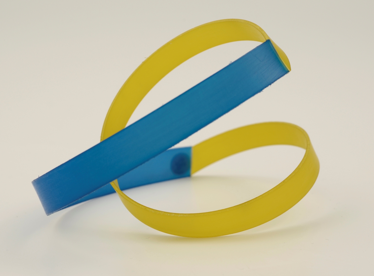 Armbånd laget av stive nylonbånd som er cirka 1 cm brede. Til en blå bue er det festet et gult tvunnet bånd.
