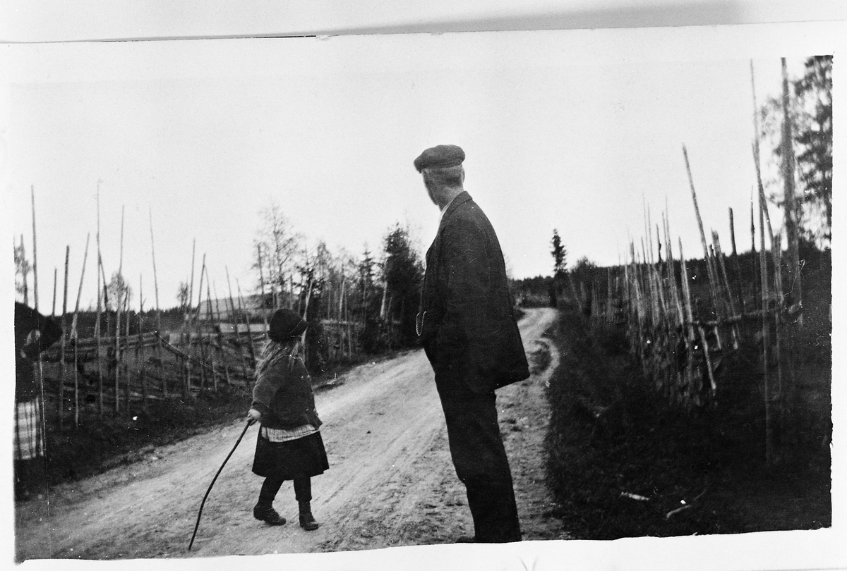 Gudrun Dahlen (Sveum) og hennes far Bernt Sveum venter på kua fra Karsrud nedre. Bak Sveum går vegen dit hvor Anton Napstads smie lå ca. 50 meter unna. Året er 1923.