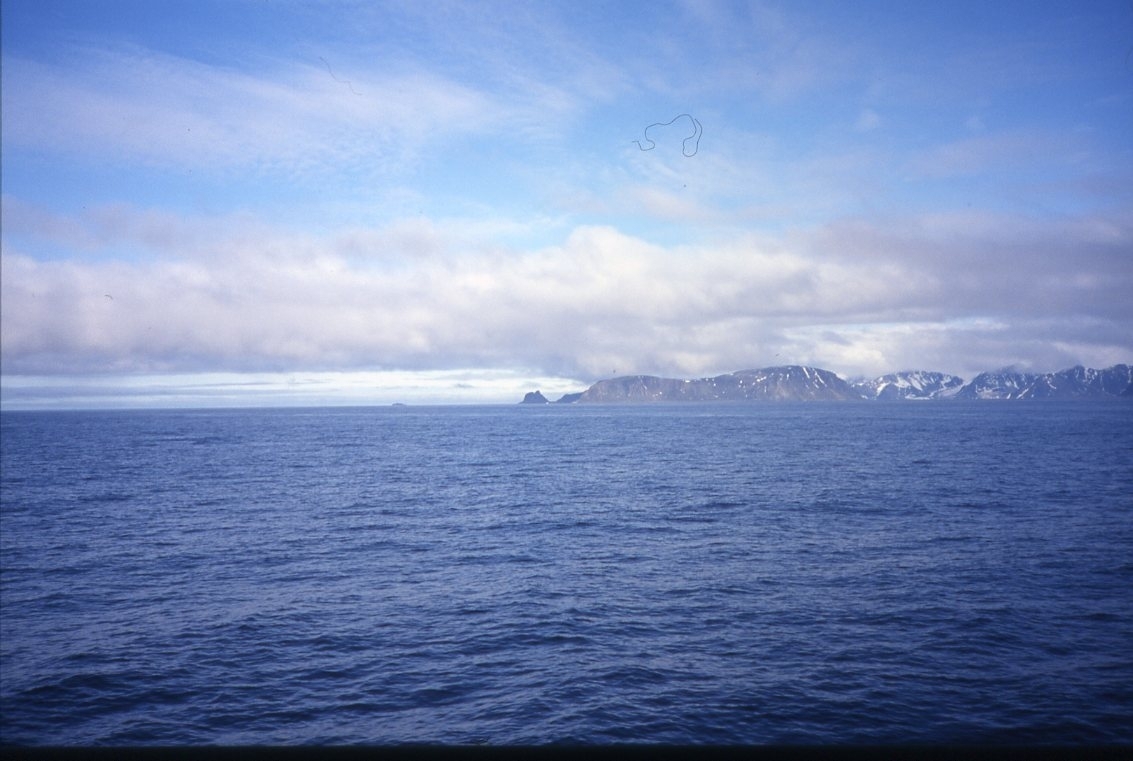 Blått hav och delvis snötäckta berg i fjärran. Sannolikt mot Danskegattet med Amsterdamön till vänster och Danskön till höger.