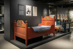 Fotografi av en rød seng i utstillingen Impulser på Maihaugen.
