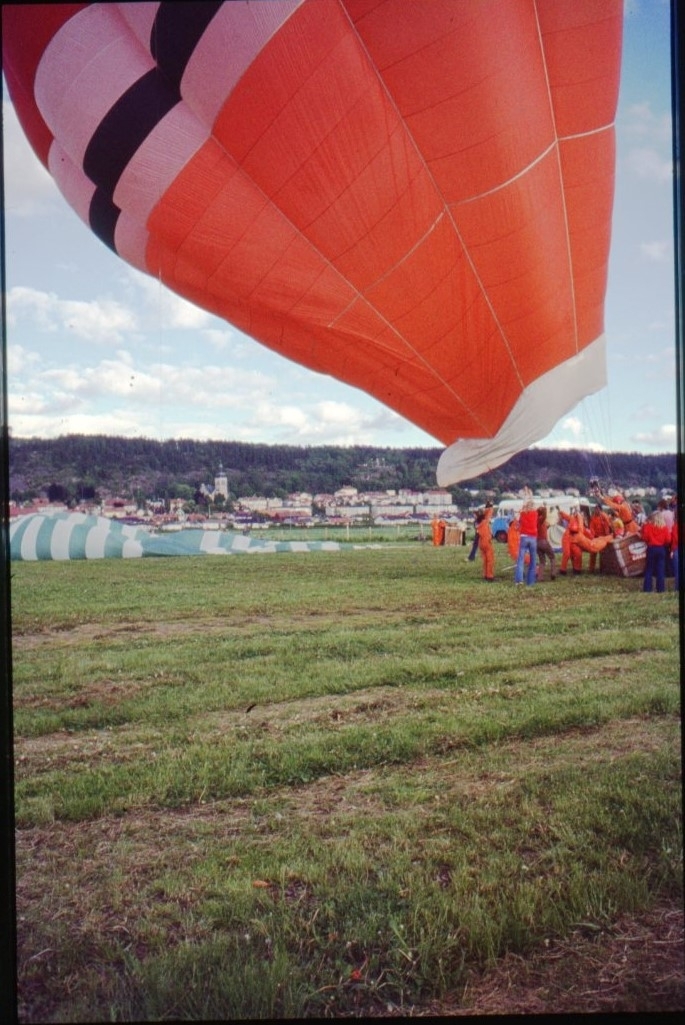 En orange-blå-vit ballong står klar att lyfta. Ballongen lutar kraftigt åt vänster.