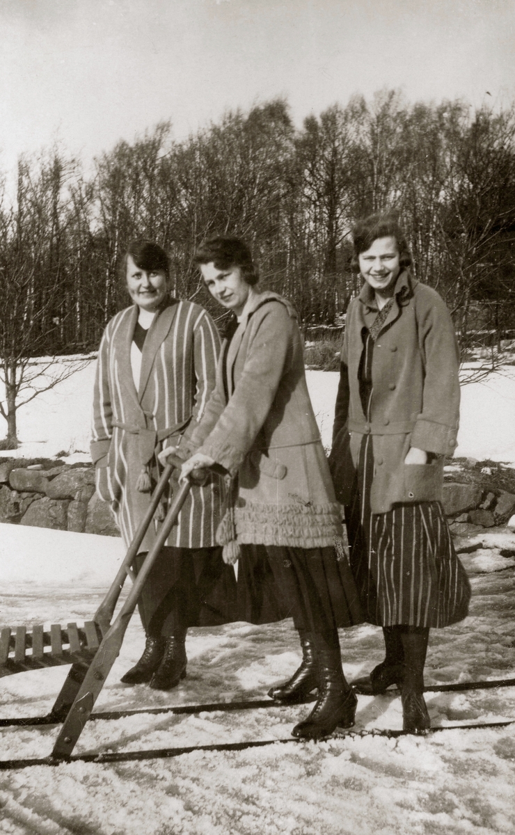 Tre kvinnor står i ett snöpudrat Kållered, 1930-tal. Från vänster: Elin Pettersson (gift Rothvall), Backen eller Högen samt systrarna Ingeborg (1901 - 1987, gift Johansson) och Astrid Gustafsson (1907 - 1994, gift Jägerström, Råda). Ingeborg och Astrid från Kållered Stom "Nygård", står tillsammans på en sparkstötting. Relaterat motiv: A3027.