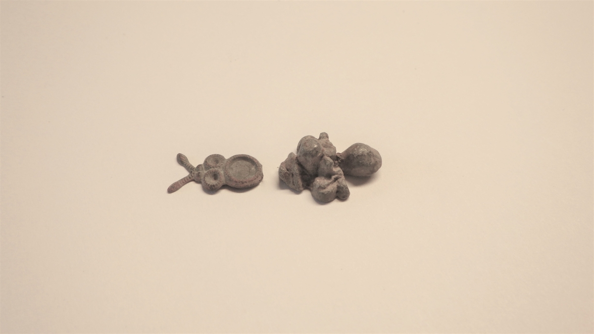 To gjenstander med bruddflater, som kan representere en eller to støpte, små figurer. Den ene, flate delen ser ut til å være noe som likner en bie. Den andre delen, som er større og kraftigere, kan representerer en annen figur eller dekordel. Det er mulig at de toi gjenstandene inneholder ulike metaller.