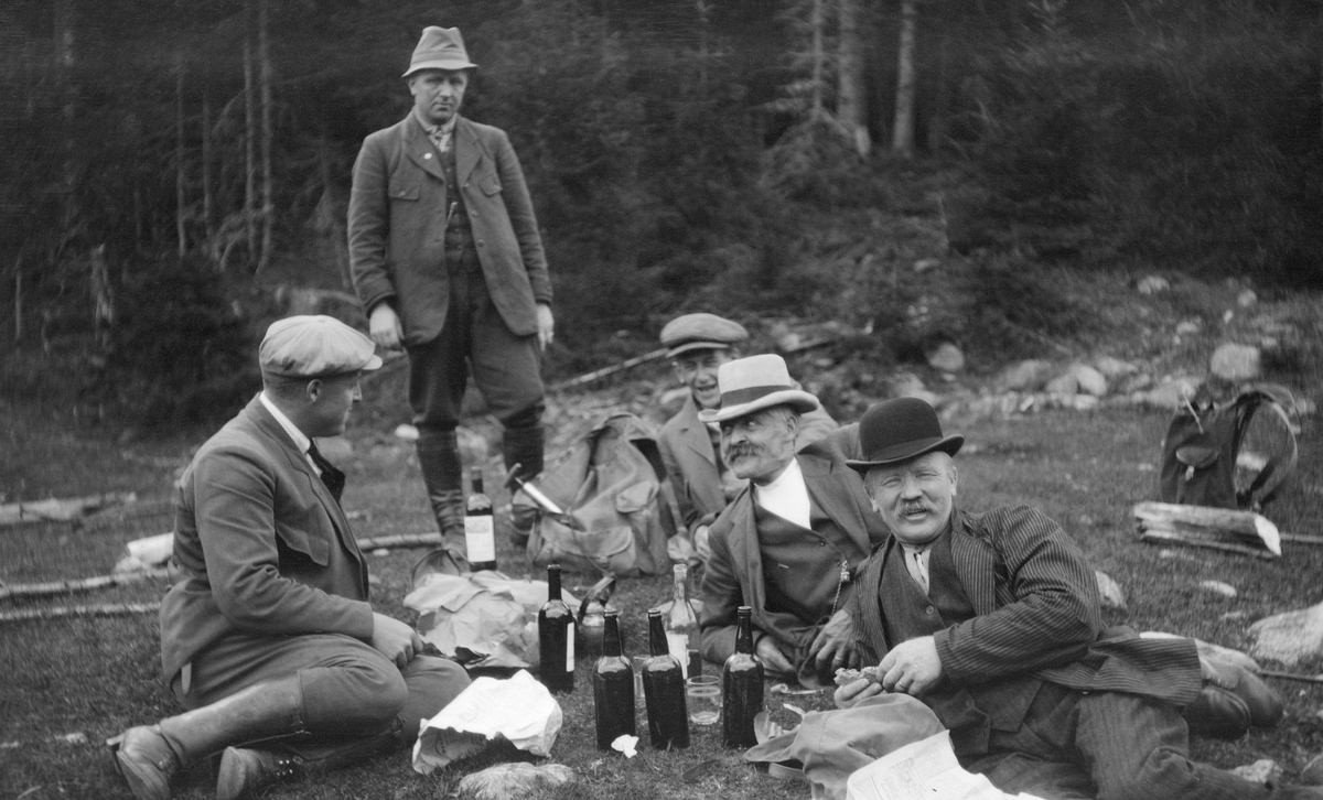 Pause under fløtingsbefaring i Agåa i Elverum kommune i Hedmark i 1919.  Fotografiet viser fem menn, antakelig skogeiere som var valgt inn i «åstyret», og som dermed hadde ansvar for å administrere fløtinga i dette sidevassdraget.  Tre av karene ligger på grasbakken, en sitter og en står.  Mellom seg har de en kaffekjel og en del flasker med drikke.  Utnistinga hadde de øyensynlig båret med seg i ryggsekker.  De avbildete mennene skal ifølge innskrifter under en kopi av fotografiet i Glomma fellesfløtingsforenings album nr. 31 være Hans Wærlien, Gudbrand G. Sveen, S. Sveen, Nils Storberget og Adolf Findsen. 

I 1919 var det innmeldt 53 421 tømmerstokker til fløting i Agåa, men det lå også 15 900 stokker igjen etter forrige års fløting. Dette tømmeret tapte seg i omsetningsverdi, og det er nærliggende å tenke seg at denne befaringa ble avviklet for å utrede hva som kunne gjøres for å redusere faren for at så mye tømmer skulle bli «inneliggende». Akkurat da fotografiet ble tatt var karene så blide at det neppe kan ha vært slike problemer de tenkte på. Fløtinga i Agåa i 1919 gikk for øvrig forholdsvis bra: Bare 921 stokker lå igjen i eller ved elva da fløterne gav seg. Dette utgjorde bare en drøy prosent av det tømmeret som skulle vært ekspedert.