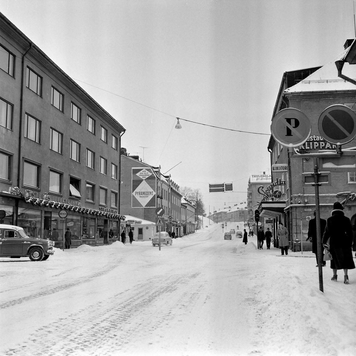 Stora gatan mot väster i korsningen med Källgatan. Aktuell byggnad skymtar på gatans vänstra sida under reklamplanschen. Byggnaden revs på 1960-talet