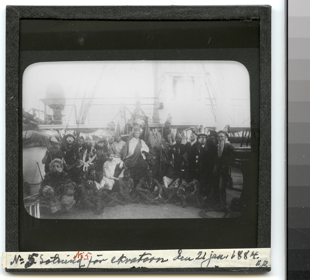 Bilden föreställer en grupp fantasifull utklädda sjömän som har samlats på däck inför neptunifesten vid passerandet av linjen den 21 jan 1884 ombord på fregatten Vanadis under hennes världsomsegling 1883-85.