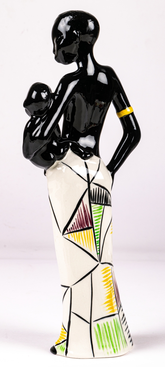 Figurin föreställande svart kvinna med ett barn på höften, flintgods, handmålad, glaserad. Djuptryck på undersida C.15 vilket står för formgivare Dorothy Clough, samt stämpeltryck med Gefles logga med tre rundugnar.