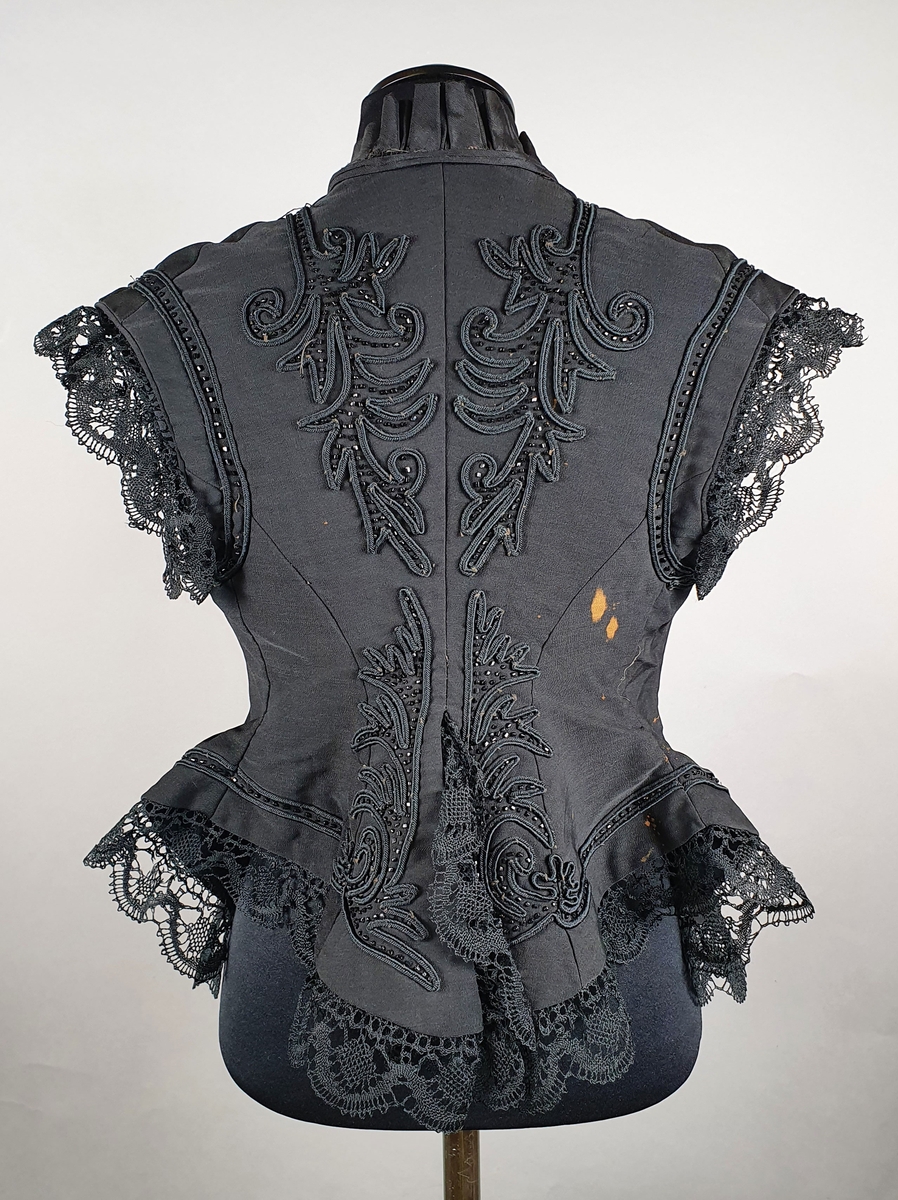 Svart ermeløs bluse av silke med lissebroderi med perler både på rygg og forstykkene. Svarte blonder langs ermekanten og nederst på livet.