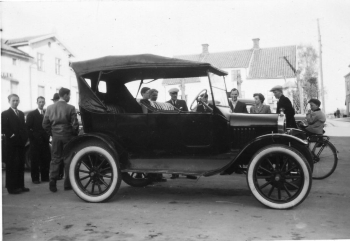 En bil med sufflett - T-ford av modell 1924-1925 - står parkerad omgiven av folk.