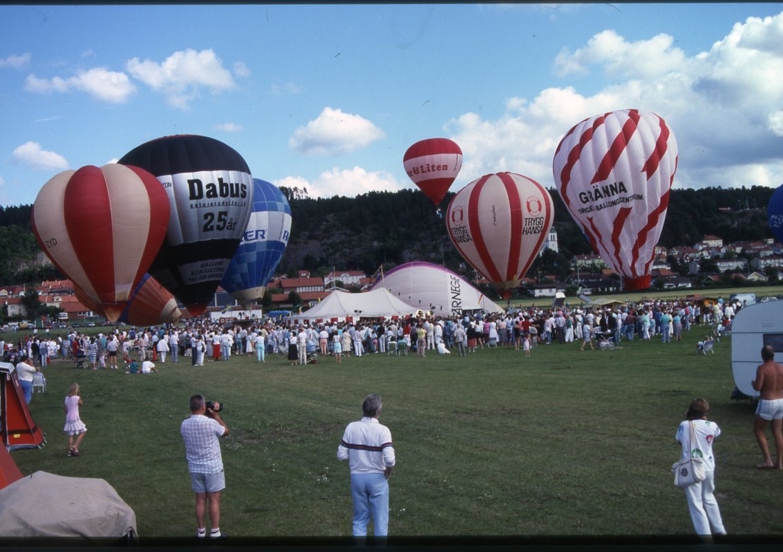 Luftballonger fylls och lyfter från en gräsplan. En stor publik.
